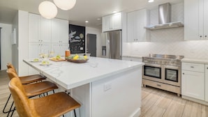 A modern kitchen with a central island, white cabinetry, stainless steel appliances, and pendant lighting. - White Agate by Avantstay Pool + Spa + Putting Green Playground + Outdoor Dining Minutes to Kierland (Scottsdale)
