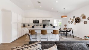 A modern kitchen with white cabinets, a central island, and a dining area with a table and chairs.