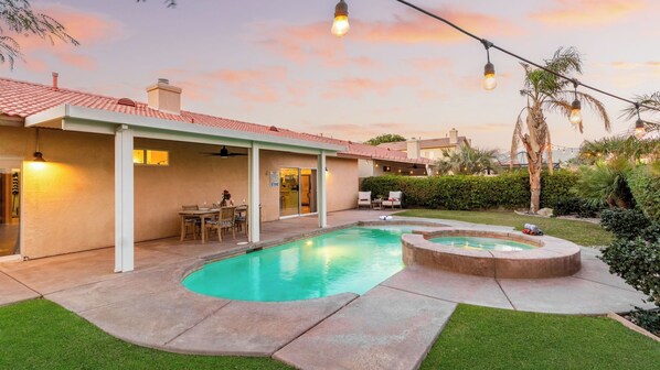 Un patio trasero con piscina, jacuzzi y zona de patio techada.