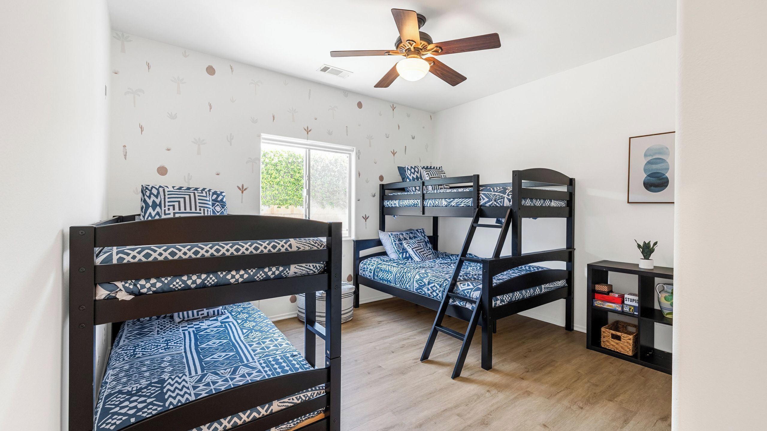 Ein Zimmer mit Etagenbetten, einem Deckenventilator, einem Fenster und einem kleinen Tisch mit einer Pflanze.