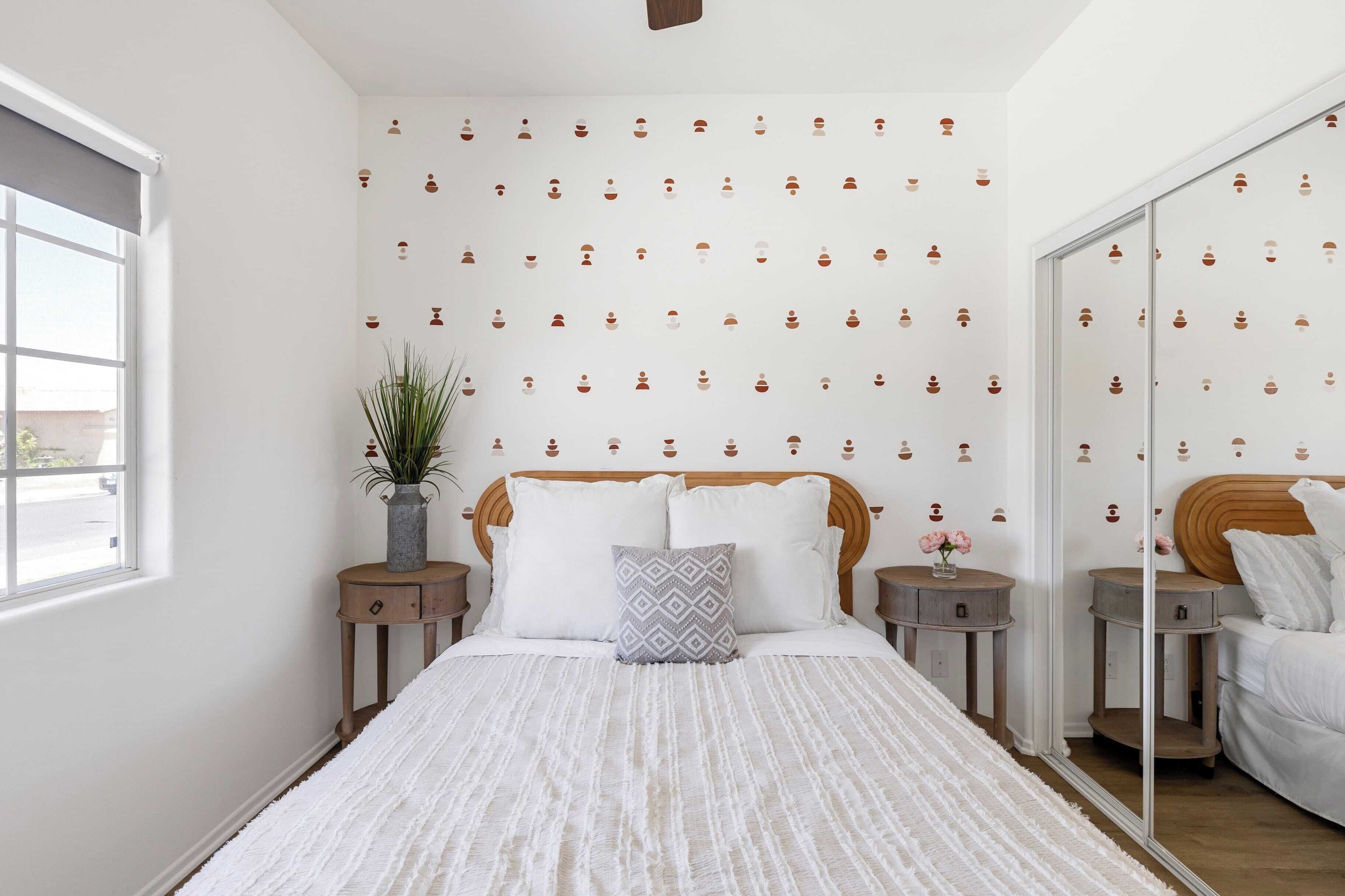 A bedroom with a large bed, a mirror, a potted plant, and a wall with a repeating pattern.