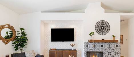 A modern living room with a sofa set, a coffee table, a fireplace, and a flat-screen TV mounted on the wall.