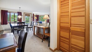 A room with a dining table, chairs, a sofa, and a wooden closet. - 2 bedroom Ski-in condo with pool, hot tub, and EV chargers. (Killington)