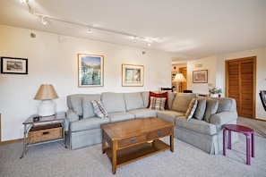 A living room with a grey sofa, a wooden coffee table, a lamp, and framed pictures on the wall.