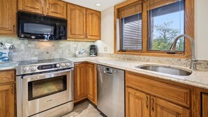 A kitchen with wooden cabinets, a stainless steel Bosch oven, a dishwasher, a microwave, and a window with blinds. - 2 bedroom Ski-in condo with pool, hot tub, and EV chargers. (Killington)