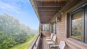 A wooden deck with white chairs and a view of a green landscape. - 2 bedroom Ski-in condo with pool, hot tub, and EV chargers. (Killington)