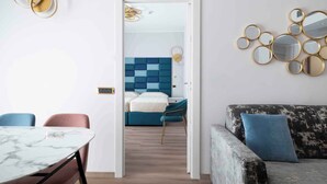 Ein modernes Hotelzimmer mit einem Marmortisch, einem Bett mit blau-weiß kariertem Kopfteil, einer blauen Couch und einer wandmontierten Spiegelanordnung.