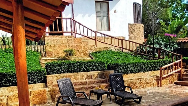 Una escalera de piedra conduce a un edificio blanco con una ventana y una puerta. Hay dos sillas negras y una pequeña mesa en un patio de piedra.