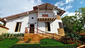 Una casa de dos pisos con balcón, escaleras y un jardín bien cuidado.