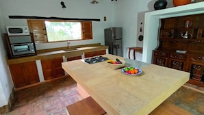 Una cocina con una isla central, microondas, tostadora, refrigerador y ventana con vista a árboles.