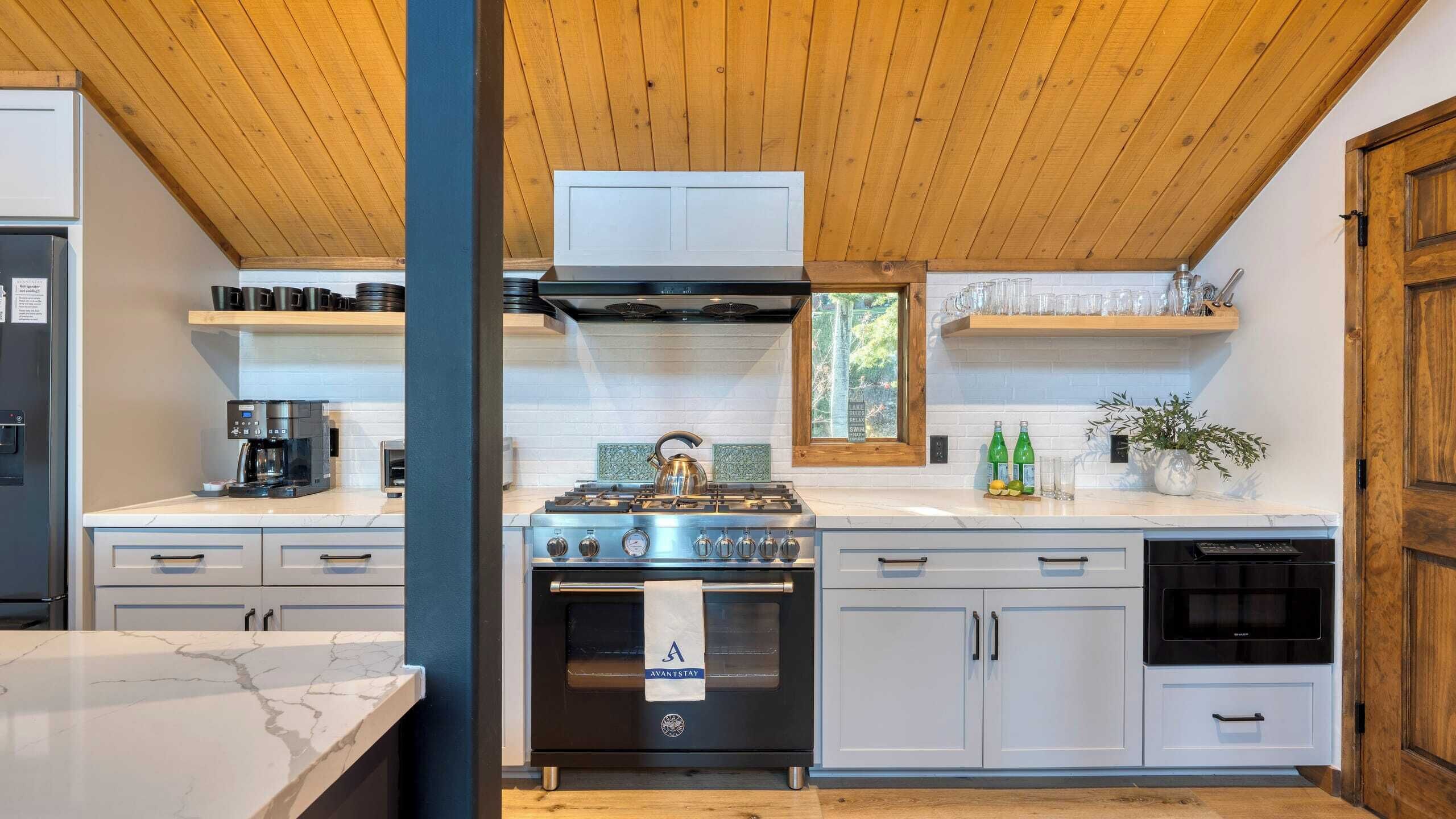 Una cocina moderna con estufa a gas, cafetera y vistas al lago a través del ventanal.