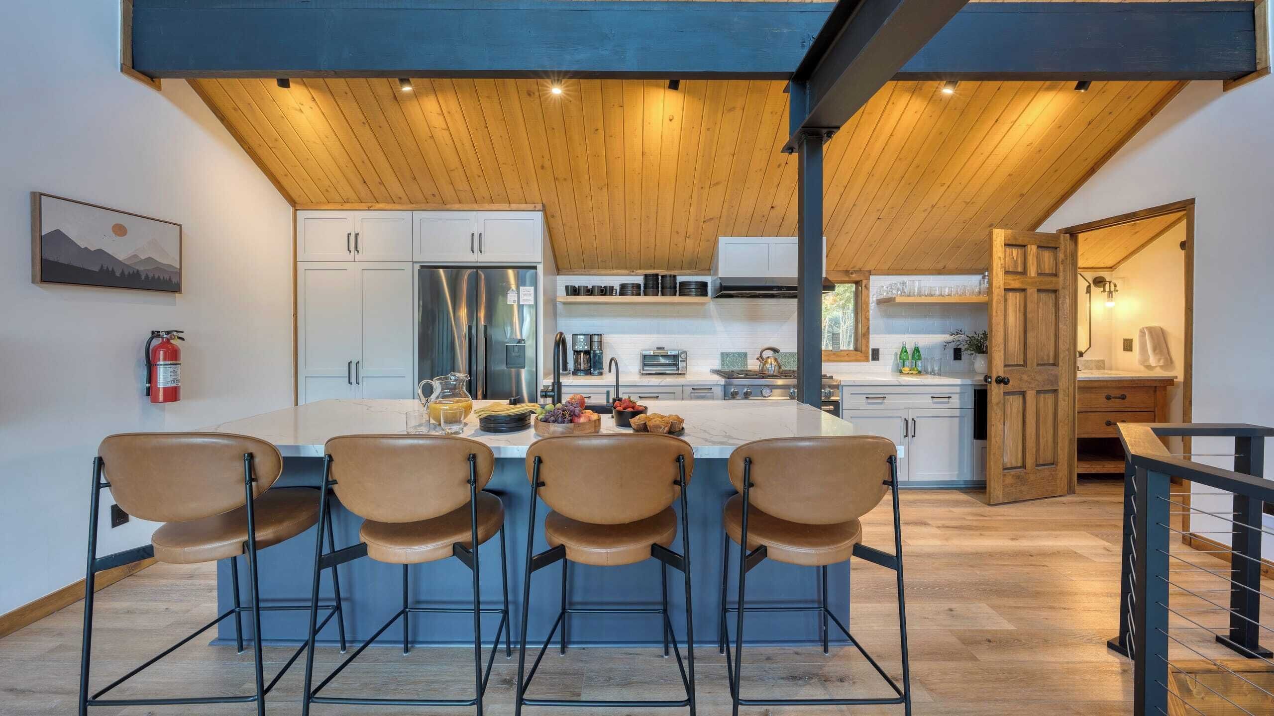A modern kitchen with a central island, bar stools, and a fire extinguisher on the wall.