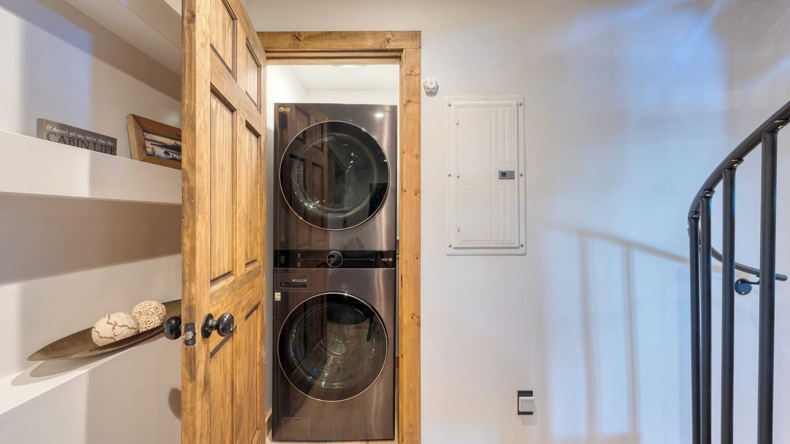 Un lavadero con dos lavadoras de acero inoxidable de carga frontal, una puerta de madera y una pared blanca con termostato.