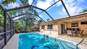 A swimming pool with a glass enclosure, surrounded by palm trees and a patio area with outdoor furniture. - 4898 4 Bedroom/2 Bathroom (Boca Raton)