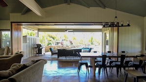 Un amplio espacio interior con una mesa y sillas de comedor, un sofá y vistas a una piscina y jardín.