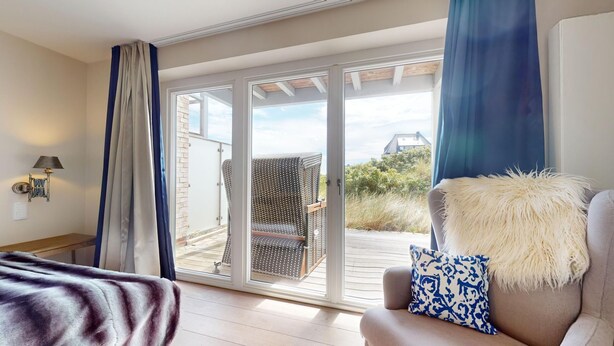 Ein Zimmer mit einer großen Schiebetür zu einem Terrassenbereich, einem Sofa mit einem flauschigen Kissen und einer Lampe auf einem Nachttisch.