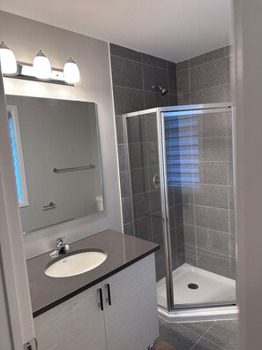 A modern bathroom with a glass shower enclosure, a vanity with a sink, and a mirror above the vanity. - Bed & Stay (Russell)