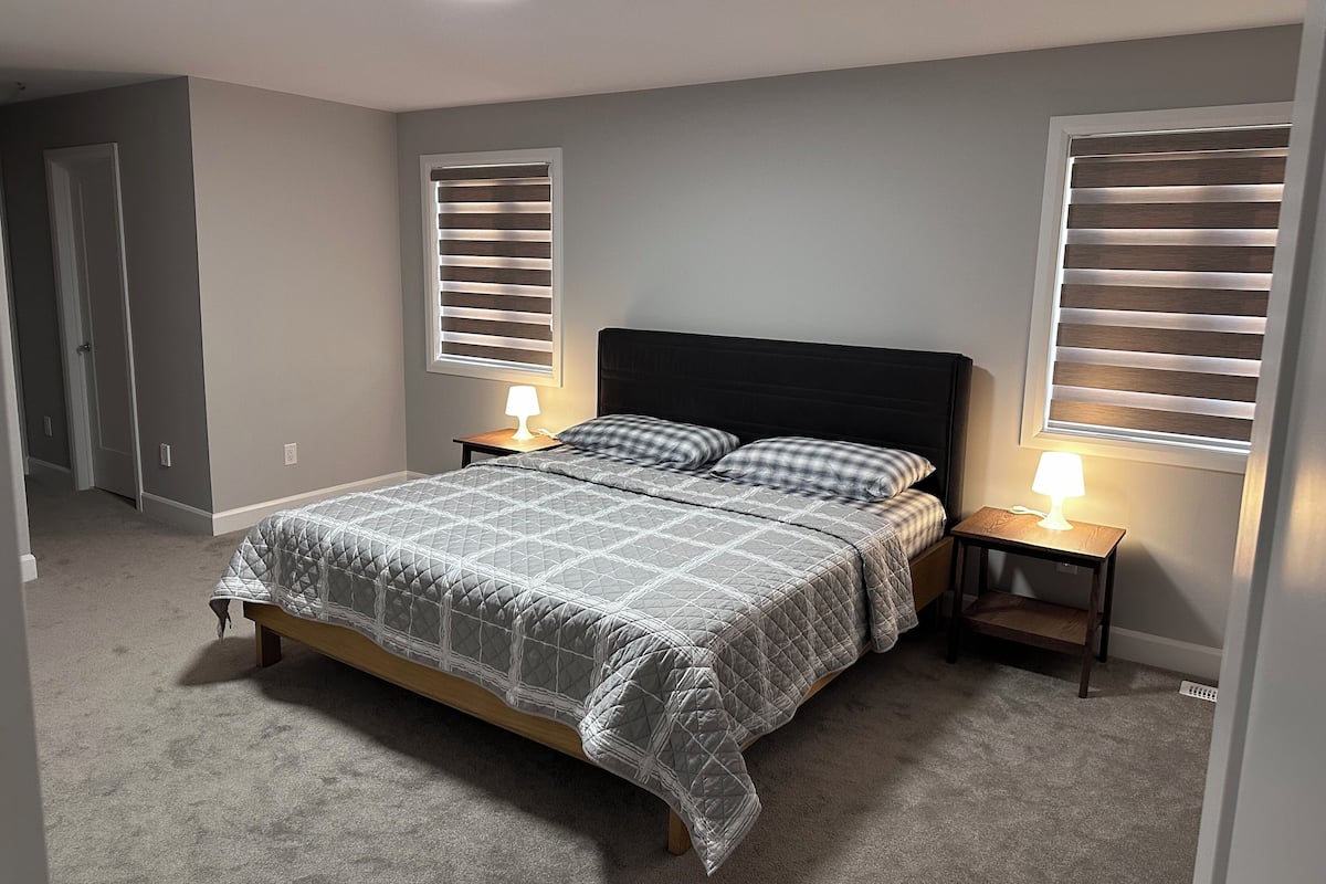 A bedroom with a bed, two bedside tables with lamps, a window with blinds, and a door.