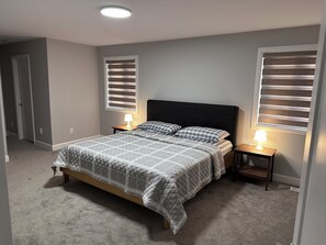 A bedroom with a bed, two bedside tables with lamps, a window with blinds, and a door. - Bed & Stay (Russell)
