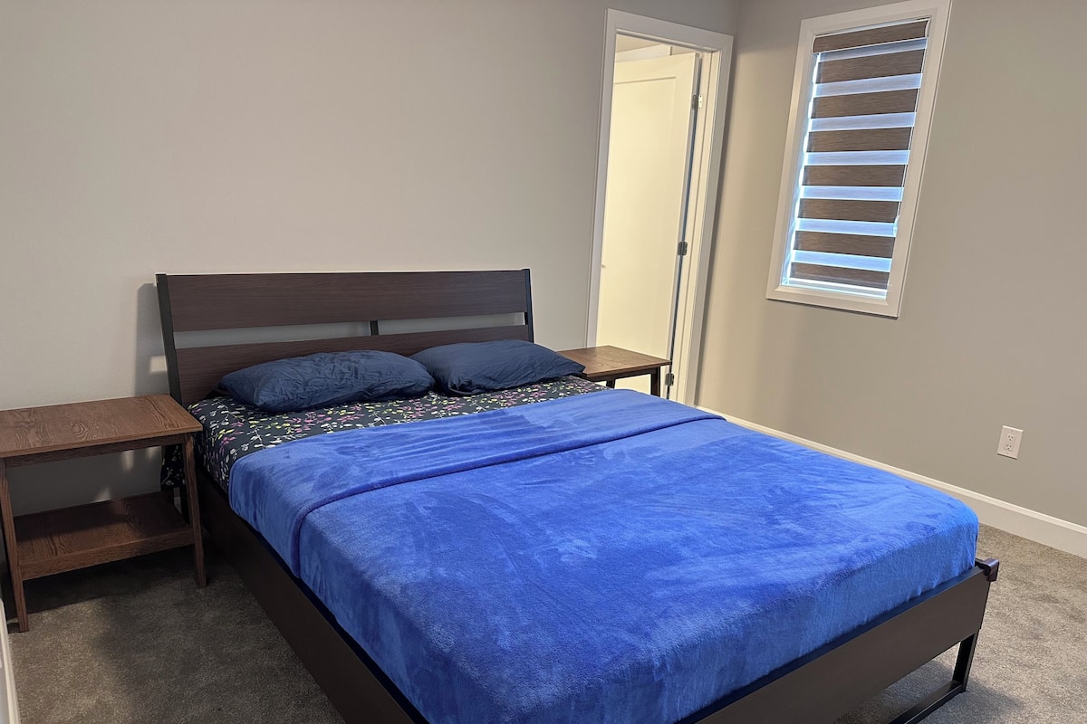 A bedroom with a bed, two nightstands, a window with blinds, and a door.