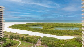 Un grand hôtel, situé dans un immeuble de grande hauteur, qui offre une vue sur une plage protégée par une mangrove, un ciel dégagé et l’océan.