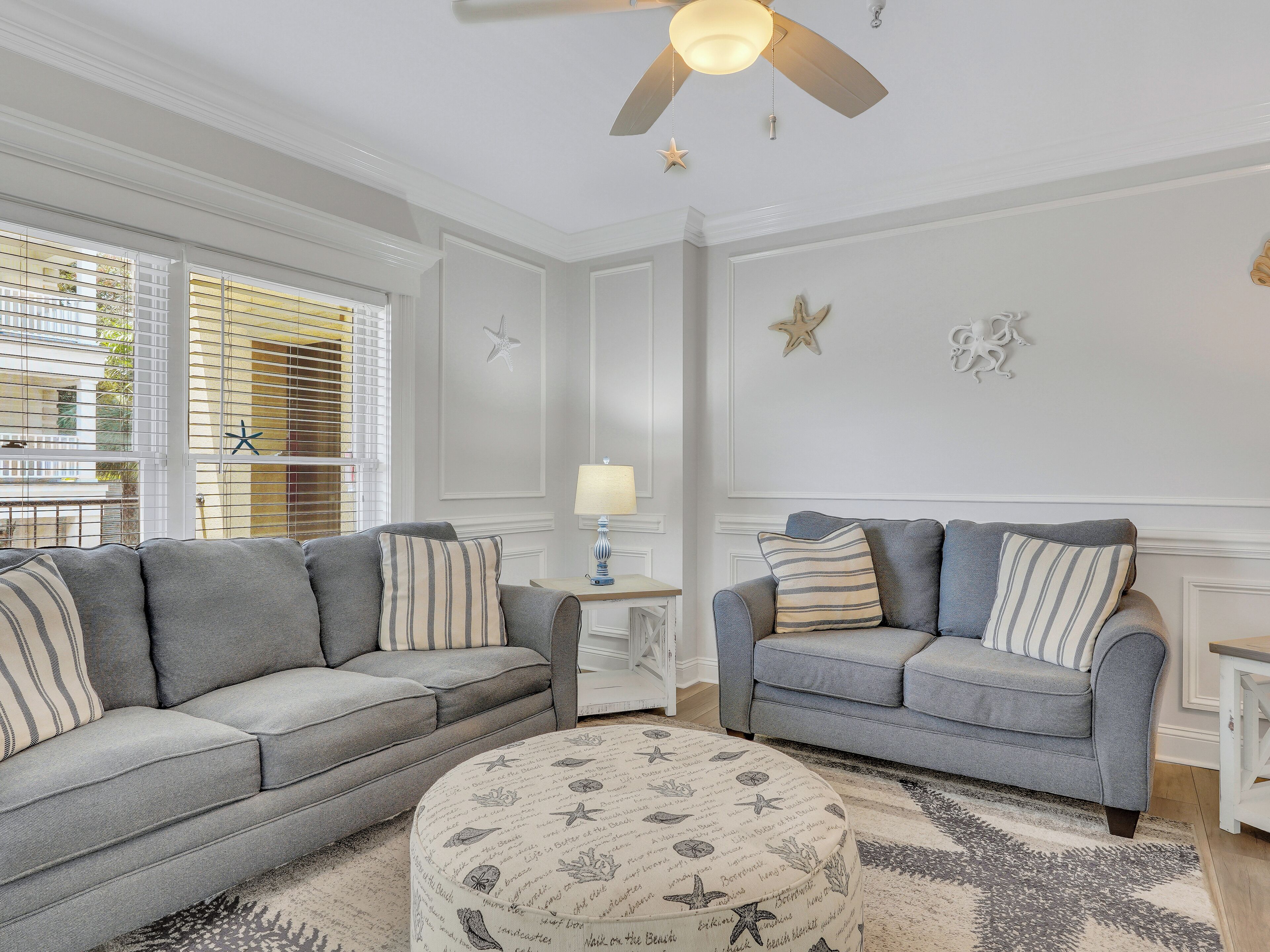A living room with two grey sofas, a round ottoman, and a ceiling fan.
