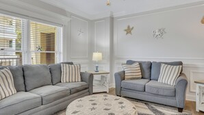 A living room with two grey sofas, a round ottoman, and a ceiling fan. - Walking Distance to Beach, Heated Pool Access (Tybee Island)