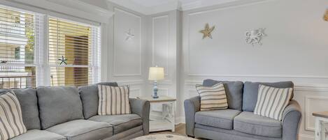 A living room with two grey sofas, a round ottoman, and a ceiling fan.