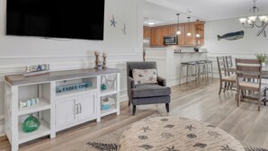 A modern living room with a flat-screen TV, a wooden console table, and a gray armchair. - Walking Distance to Beach, Heated Pool Access (Tybee Island)