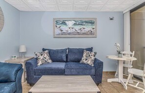 A living room with a blue sofa, a coffee table, a painting of birds on the wall, and a small round table with chairs.