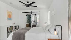 A modern bedroom with a bed, bedside table, and a reading lamp. There is a bookshelf and a mirror in the background. - Office, Patio, Yard, Pet Friendly, Playground (Austin)