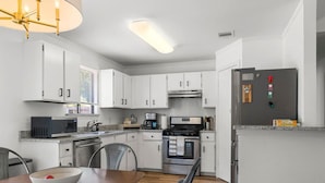A modern kitchen with white cabinets, a wooden dining table, and stainless steel appliances. - Office, Patio, Yard, Pet Friendly, Playground (Austin)