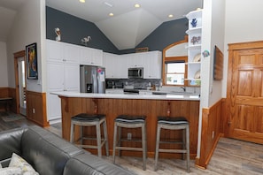 A modern kitchen with white cabinets, a central island with stools, a refrigerator, and a microwave. - Seaducktion - Spacious, oceanfront home with panoramic views and Private Pool! (Duck)