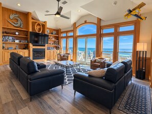 A spacious living room with a fireplace, a large TV, and a balcony with ocean views.