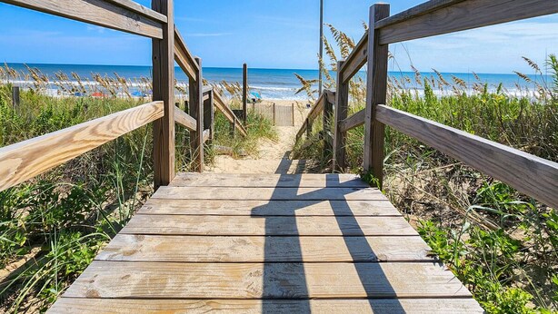 Eine Holzpromenade, die zu einem Strand führt, mit freiem Blick auf das Meer.