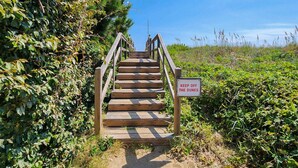 Eine Holztreppe führt zu einem Strandabschnitt. Ein Schild steht dort und trägt die Aufschrift 'KEEP OFF THE DUNES'.