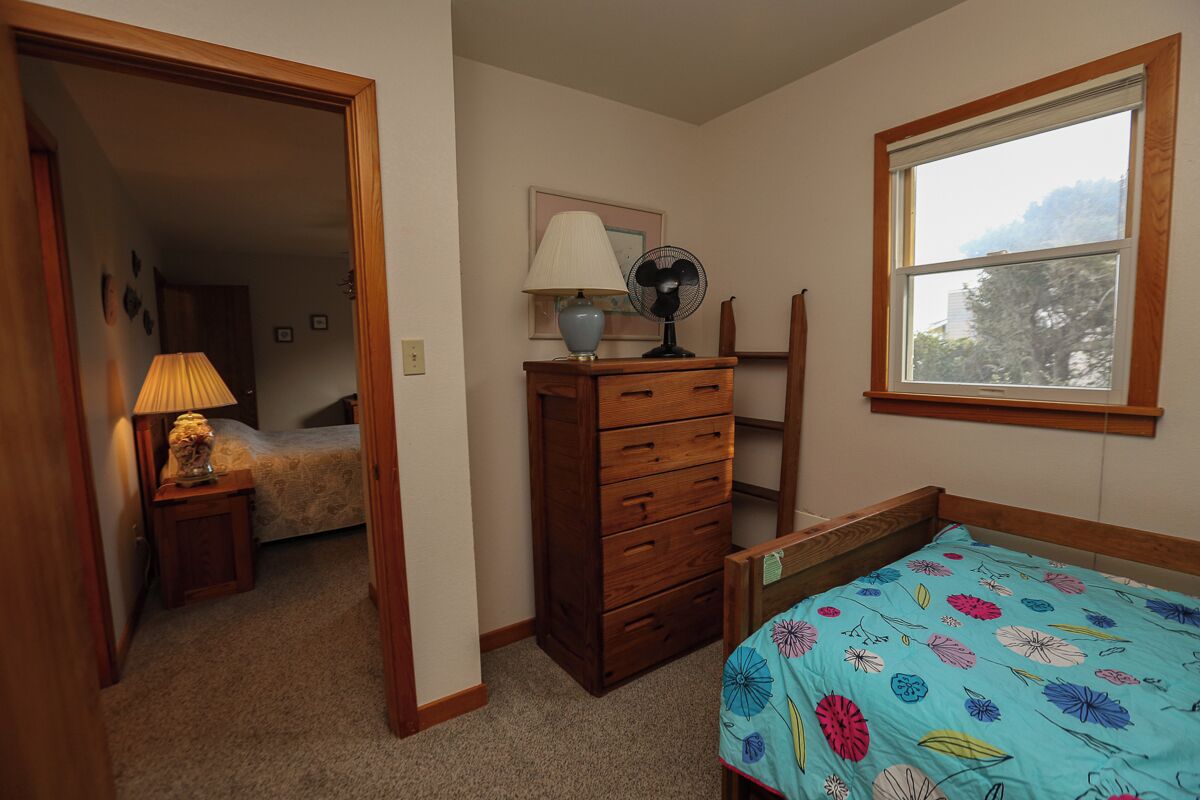 A bedroom with a bed, a dresser, a nightstand, a lamp, a fan, and a window.