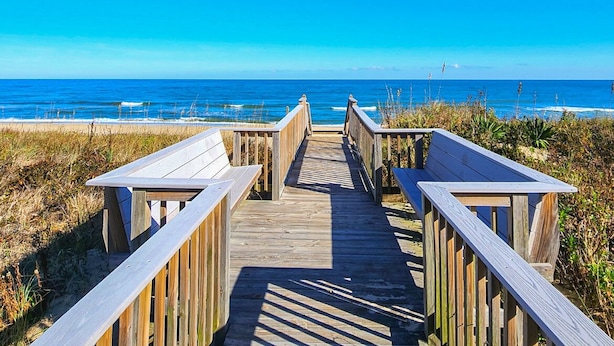 A wooden boardwalk leading to a beach with clear skies.