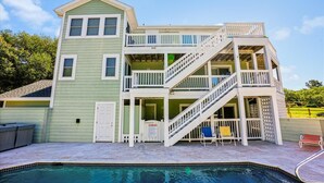 Una casa de dos pisos con piscina, un porche cubierto y una escalera que sube al nivel superior.