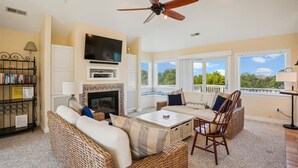 Una sala de estar con chimenea, televisor, ventilador de techo y vistas al exterior.