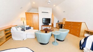 Habitación de hotel con sofá, dos sillones, una mesita, televisor, armario y ventilador de techo.