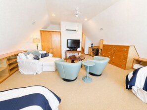 Habitación de hotel con sofá, dos sillones, una mesita, televisor, armario y ventilador de techo.