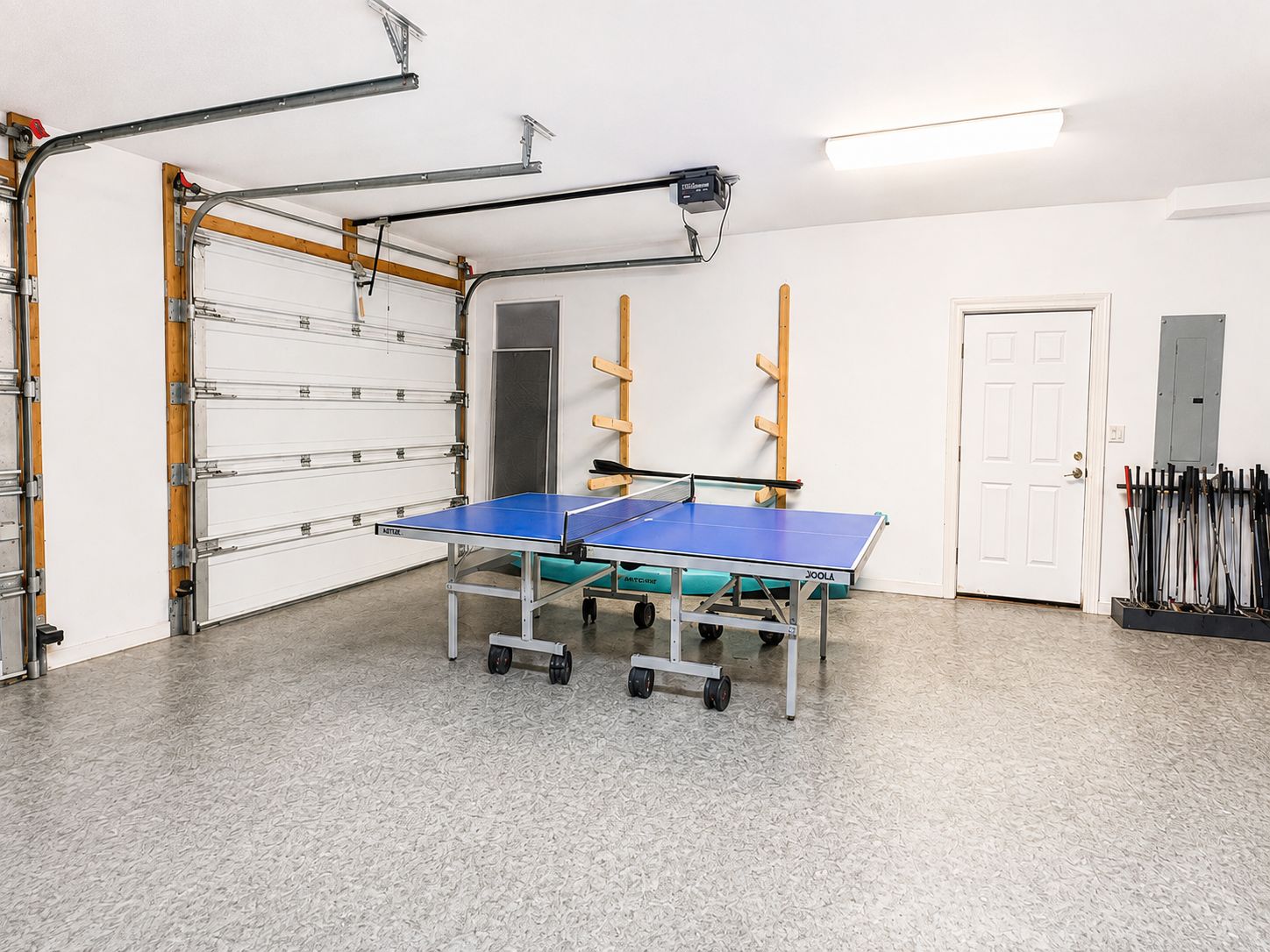 A ping pong table in a room with a white door, a white ceiling, and a white wall.
