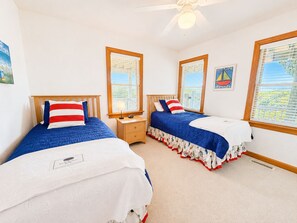 Une chambre avec deux lits, une table de chevet, un ventilateur de plafond et une fenêtre avec des stores.