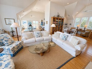 A spacious living room with a high ceiling, a glass coffee table, and a large bookshelf.
