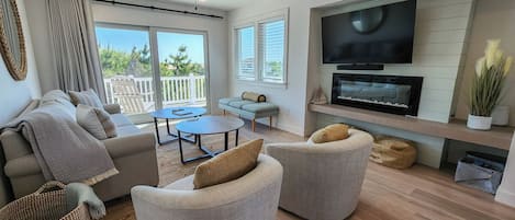 Ein modernes Wohnzimmer mit Flachbildfernseher, grauen Sofas, einem Couchtisch und einem Balkon mit weißen Geländern.