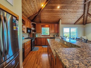 Eine Küche mit Holzausstattung, einem Edelstahlkühlschrank, Granit Arbeitsplatten und einer Holzkοννe.