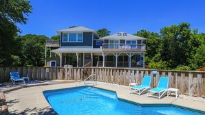 A two-story house with a swimming pool and deck chairs.