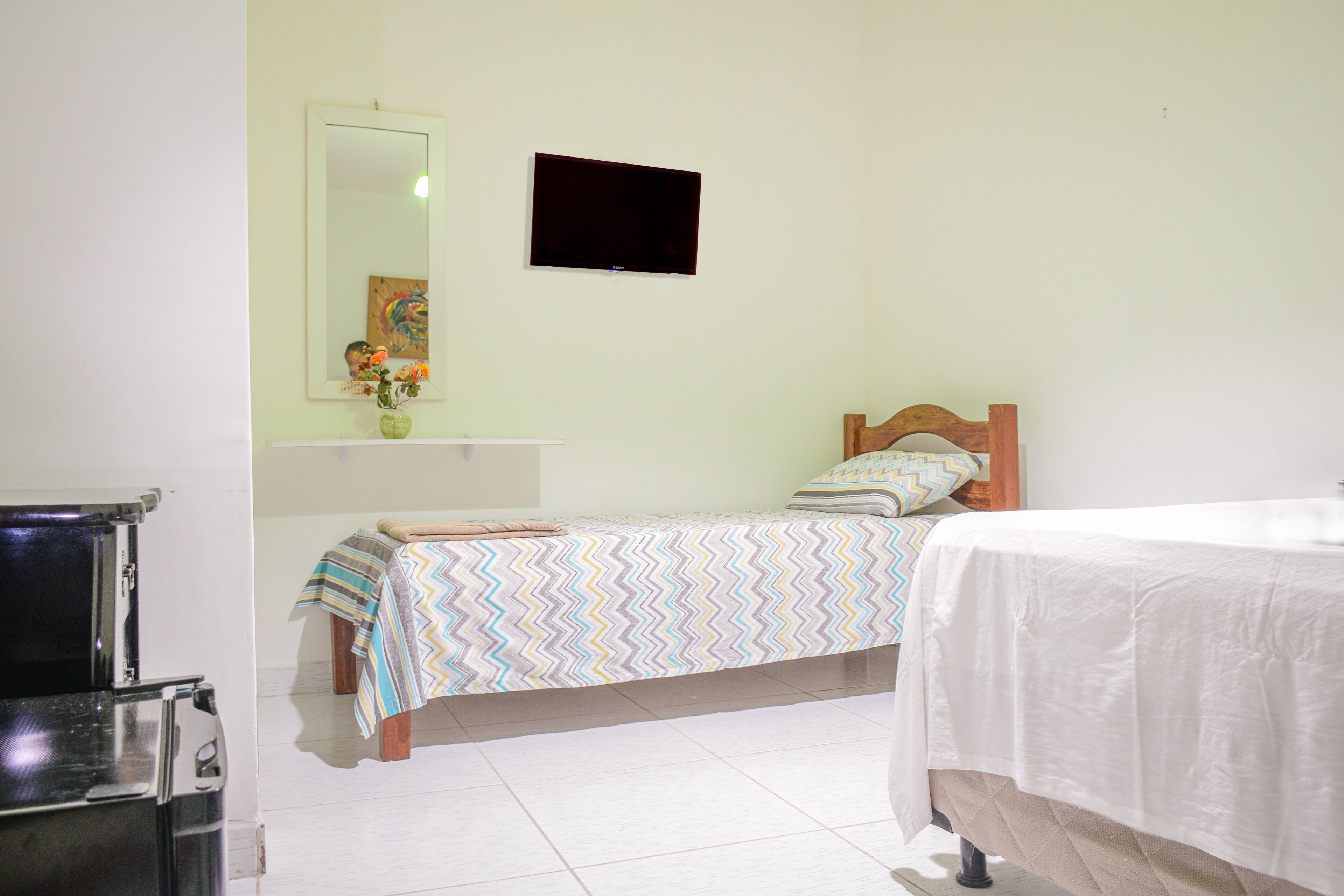 A bedroom with a bed, a TV, a mirror, and a small table with a vase.