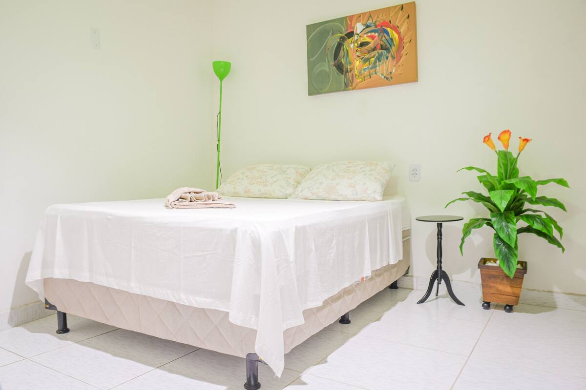Un dormitorio con cama, una mesita de noche, una lámpara de pie verde, una pequeña mesa redonda y una planta en maceta.